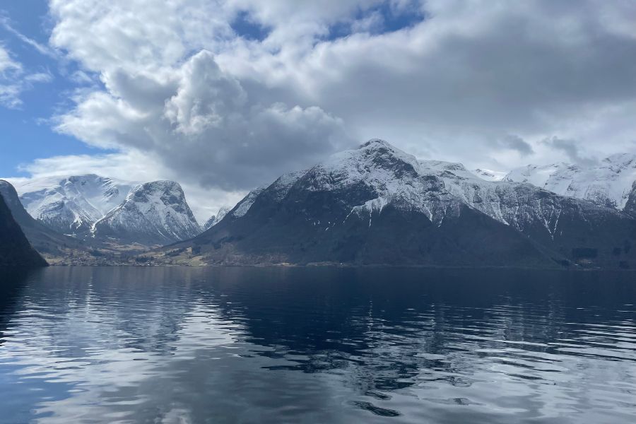 The view from a Norwegian ferry: fjords, snow-capped mountains, and clouds.