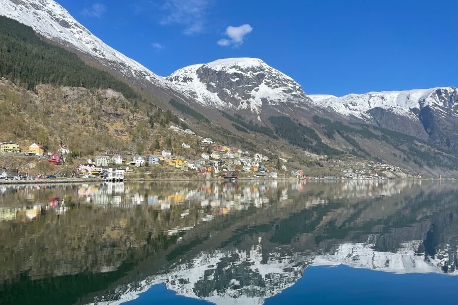 Snowy mountains and a small colorful town reflect in the fjord near the bus station on Odda, Norway.