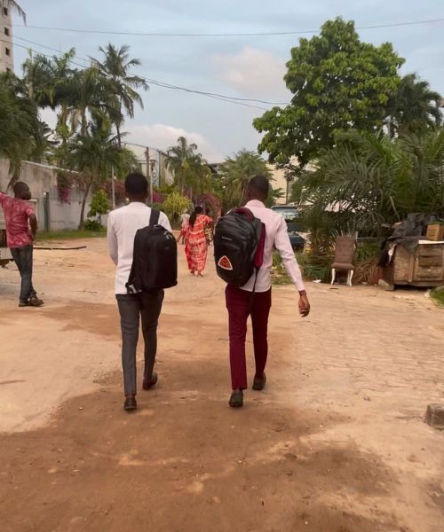 A pair of well-dressed men walk on a dirt road in  Zone 4, a neighborhood in Abidjan, Côte d'Ivoire.