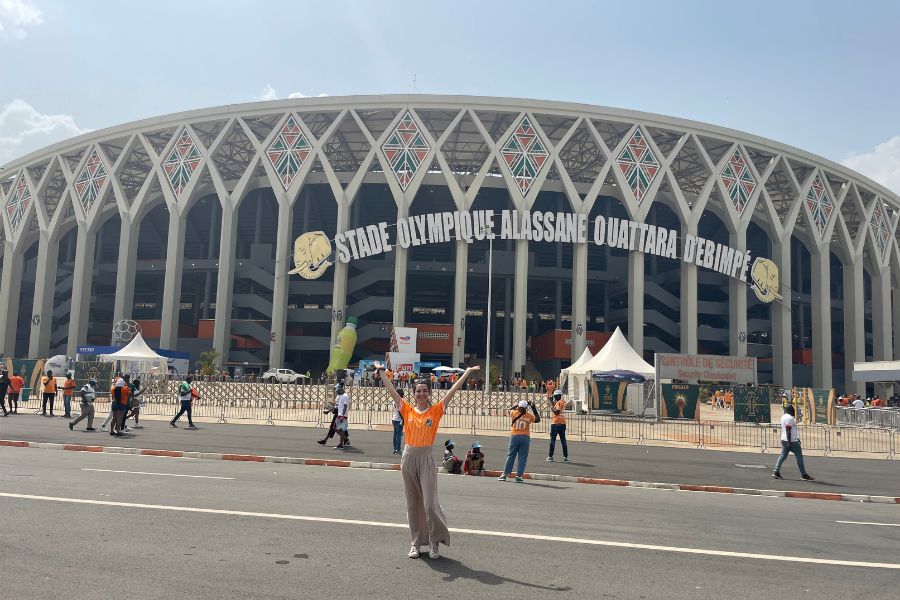 A young white girl poses in an orange football jersey poses in front of the Abidjan stadium before the final match of AFCON 2024